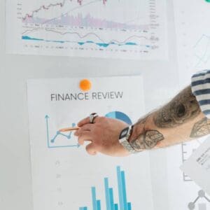 A person with tattoos pointing to finance review on paper.